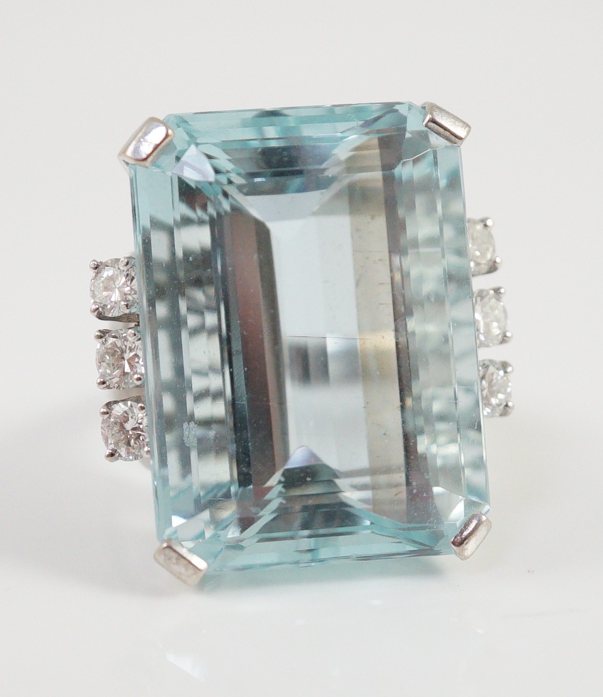 A large modern 14k white gold and emerald cut aquamarine set dress ring, flanked by six round cut diamonds